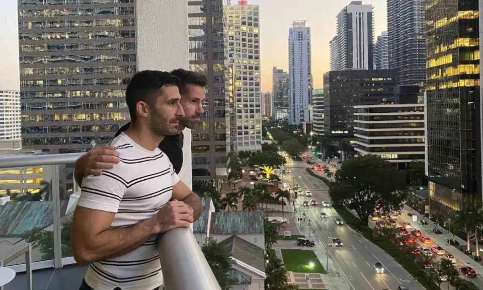 Two men embrace on a balcony overlooking a city street, a scene reminiscent of some of the most gay cities in the US.