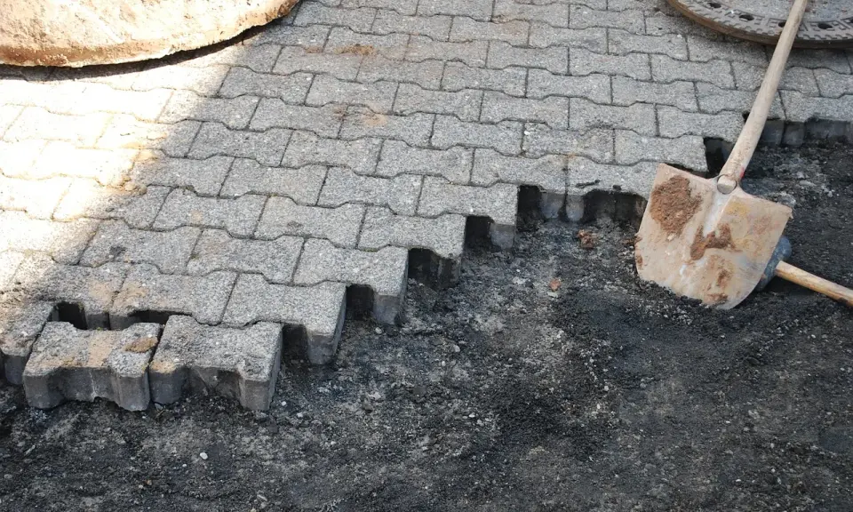 Fragment nawierzchni z kostki brukowej w trakcie układania, obok łopata.