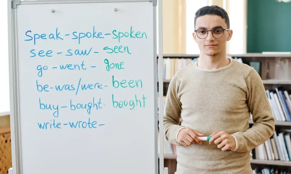 Nauczyciel wyjaśnia formy czasowników, od prostych do tych w **far stopień wyższy i najwyższy**.