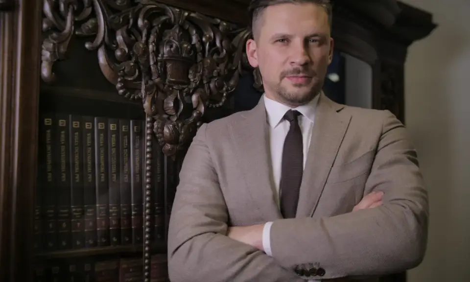 Mężczyzna w garniturze stoi przed regałem z książkami.