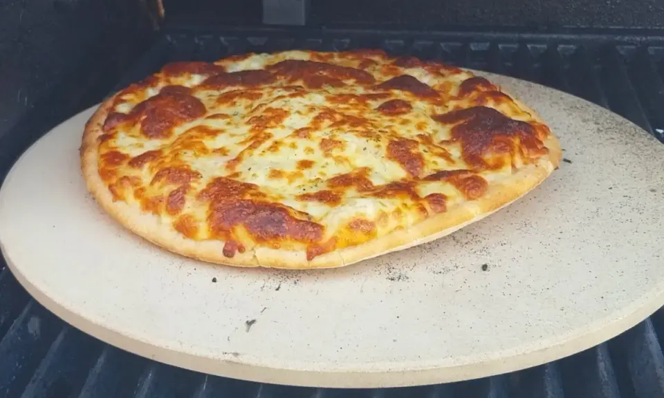 Upieczona pizza z roztopionym serem na kamieniu do pizzy na grillu.