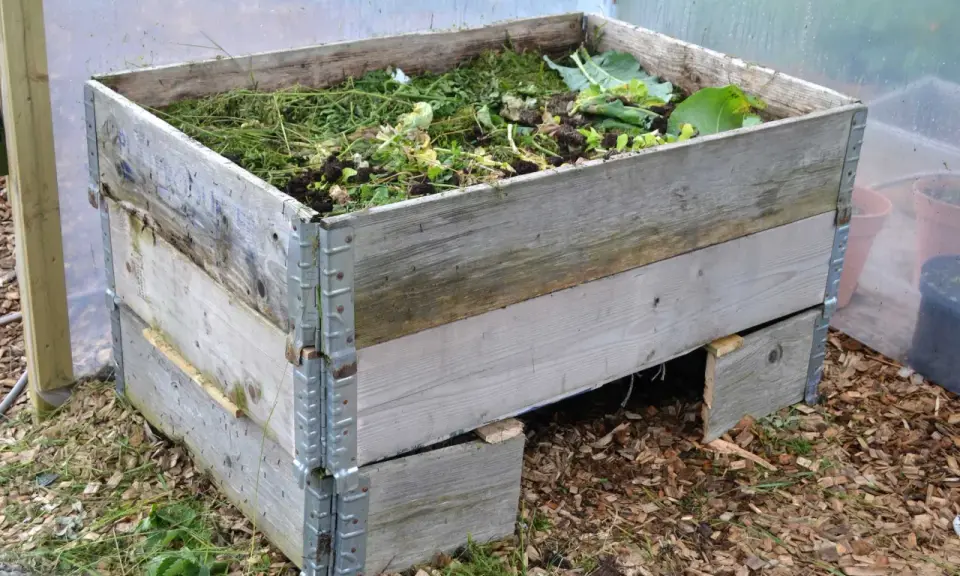 En kompost pallkrage fylld med grönt avfall och jord. Den gamla träkonstruktionen är robust och redo att omvandla trädgårdsrester till näringsrik kompost.