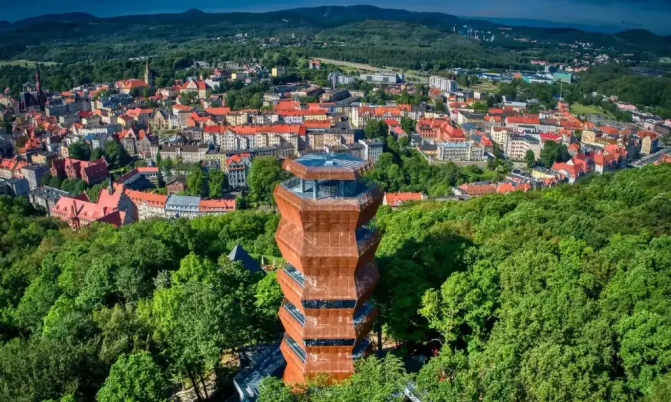 Nowoczesna wieża widokowa w otoczeniu zieleni, z panoramą miasta i Gór Wałbrzyskich w tle.