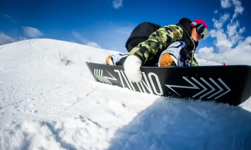 Snowboardzista w kamizelce moro i różowej czapce, zjazd na desce. Warto wiedzieć, jak dobrać buty snowboardowe, by czuć się pewnie na stoku.