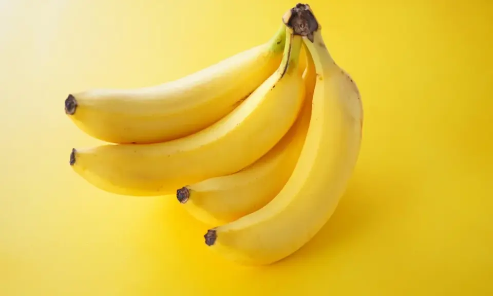 Pęczek żółtych bananów na jasnym, żółtym tle.
