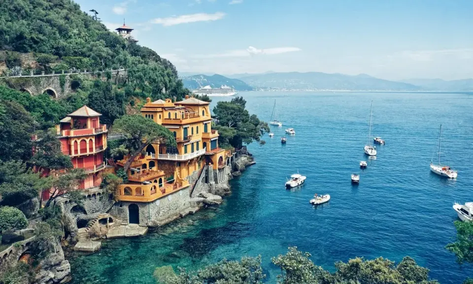 Bunte Villen am Hang über dem türkisfarbenen Meer bei Portofino, Italien. Boote schaukeln sanft auf dem Wasser.