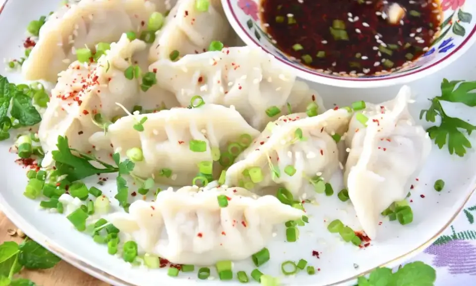 Pierożki gyoza, posypane szczypiorkiem i sezamem, podane z sosem.