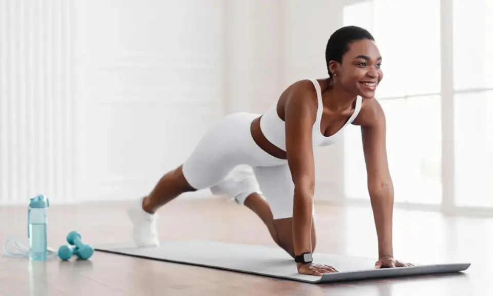 Eine Frau in weißer Sportkleidung macht eine Plank-Übung auf einer Matte. Sie zeigt, was ist gymnastik: Kraft, Ausdauer und Freude an Bewegung.