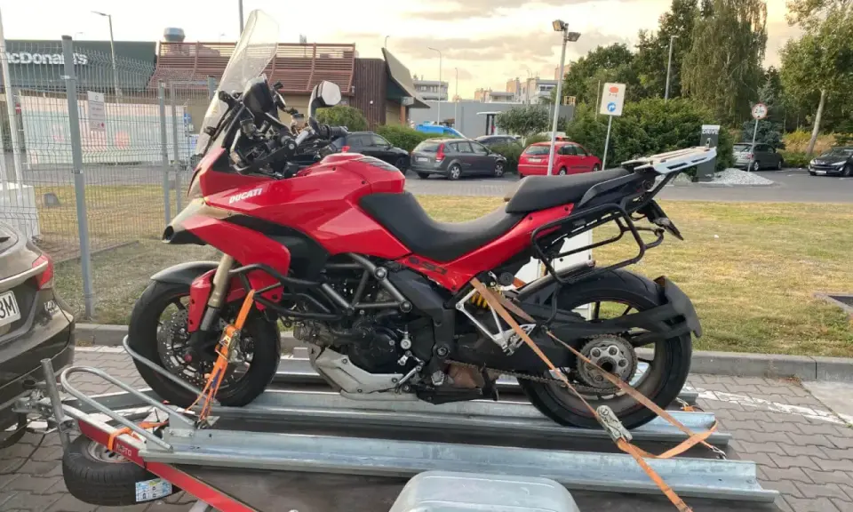Czerwony Ducati na przyczepie, zabezpieczony pasami do transportu. Gotowy do drogi.