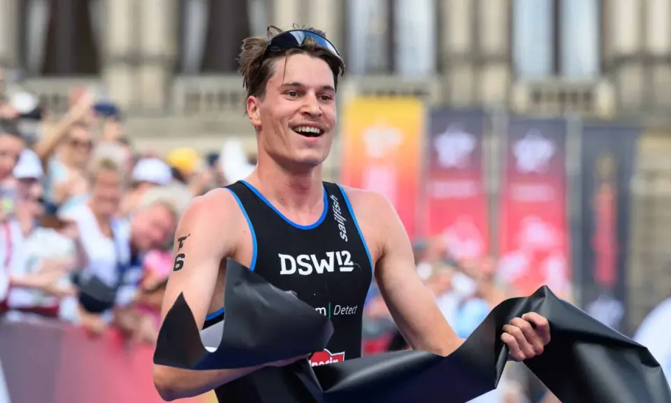 Lächelnder Athlet durchbricht die Ziellinie beim Triathlon Sprint, jubelnd mit schwarzem Band.