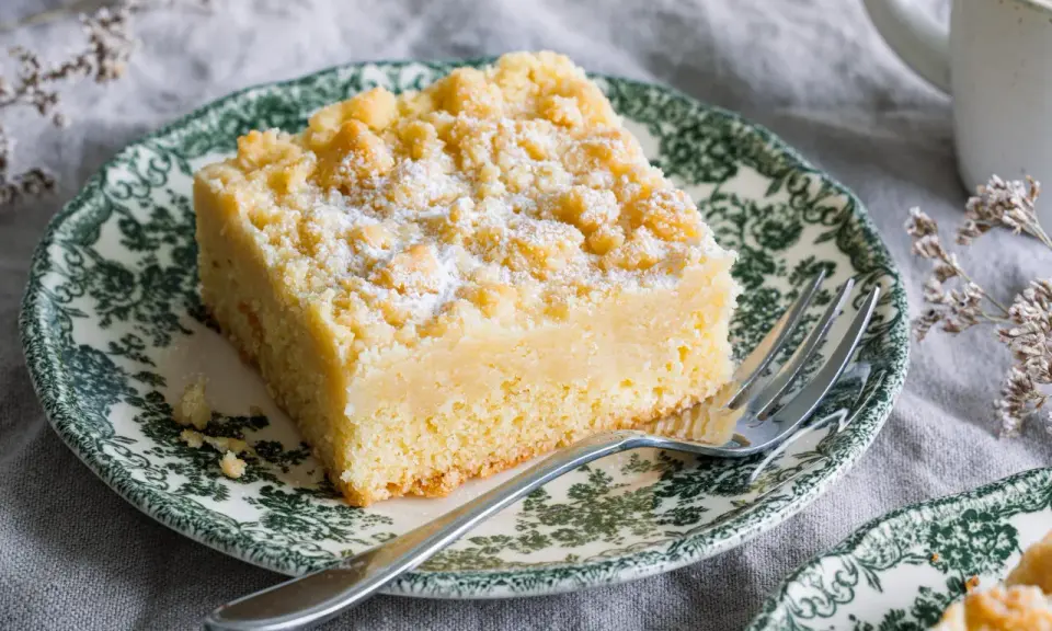 Ein Stück Streuselkuchen ohne Hefe, bestäubt mit Puderzucker, auf einem Teller mit grünem Muster.