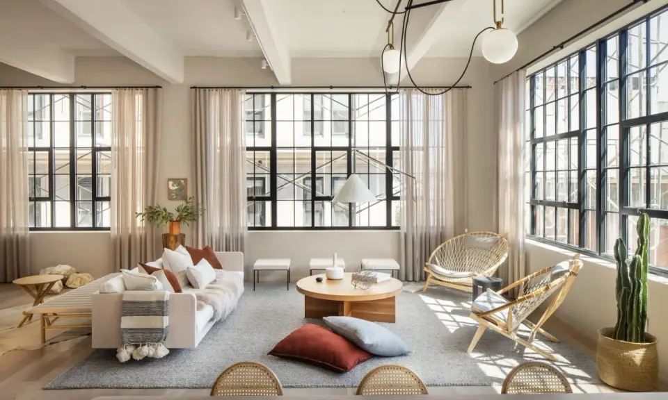 Salón con estilo industrial nórdico: sofá blanco, mesas de centro de madera, sillas de ratán y grandes ventanales.