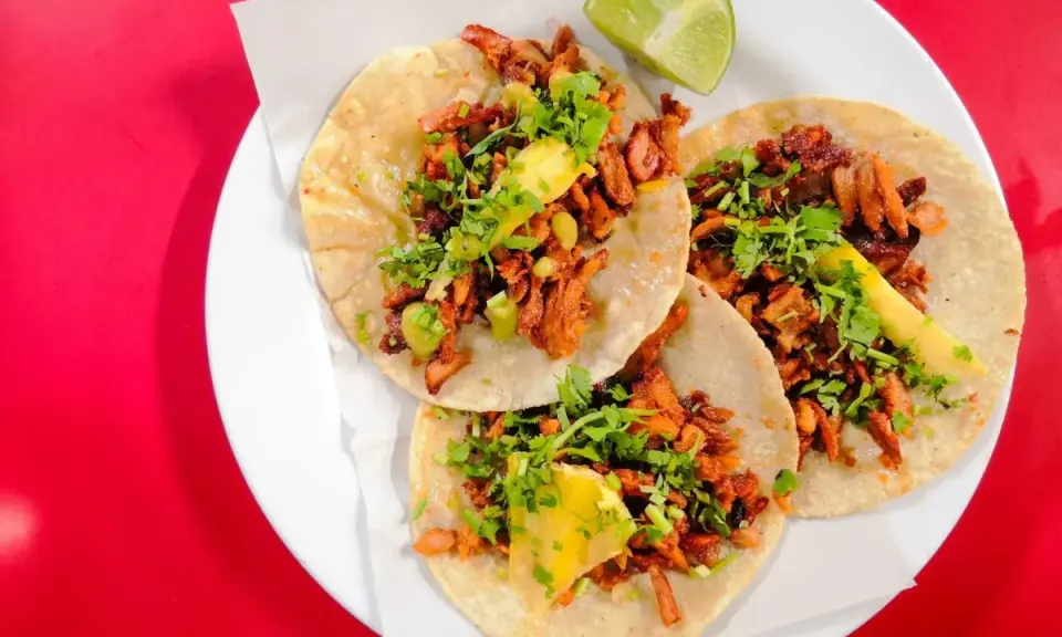 Tres deliciosos tacos al pastor, con cilantro, piña y un toque de limón, listos para disfrutar.