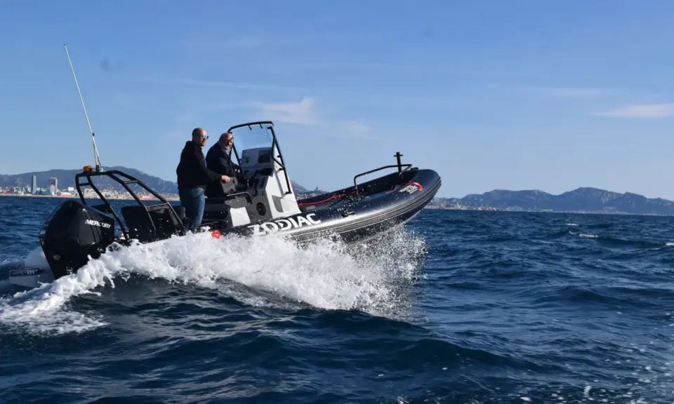 Deux hommes en Zodiac effectuent une navigation mer, projetant des embruns sous un ciel bleu.