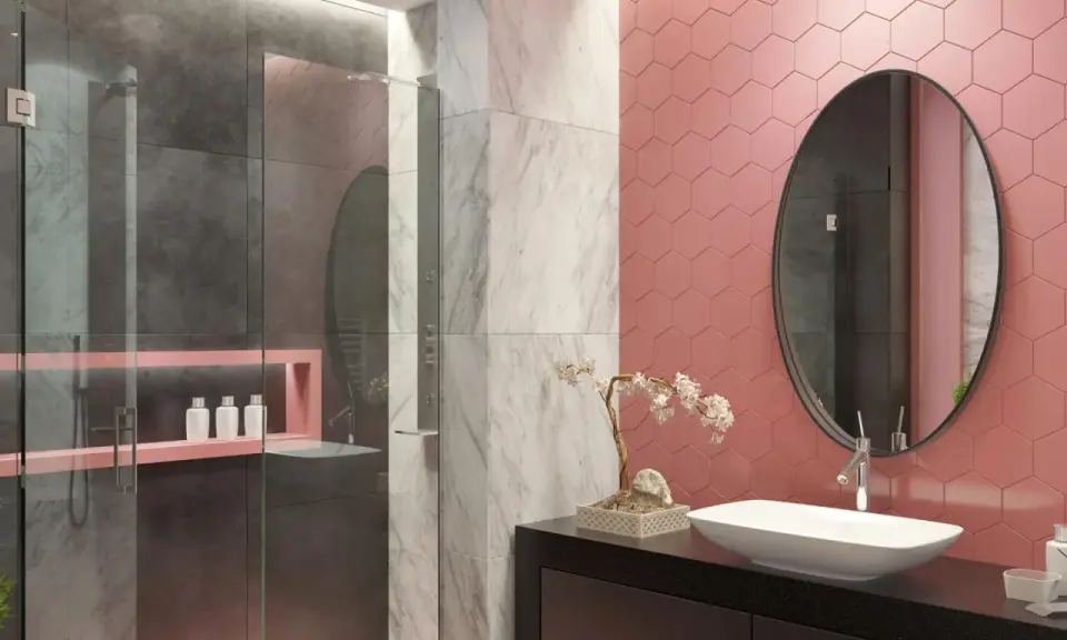 Bagno moderno con pareti rosa a nido d'ape, doccia in vetro e marmo. Un lavabo ovale su mobile nero e specchio rotondo completano le idee bagno rosa.