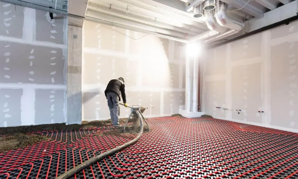 Un ouvrier installe un système de chauffage au sol hydraulique. Des tuyaux rouges serpentent sur une grille noire, prêts à diffuser une chaleur douce.