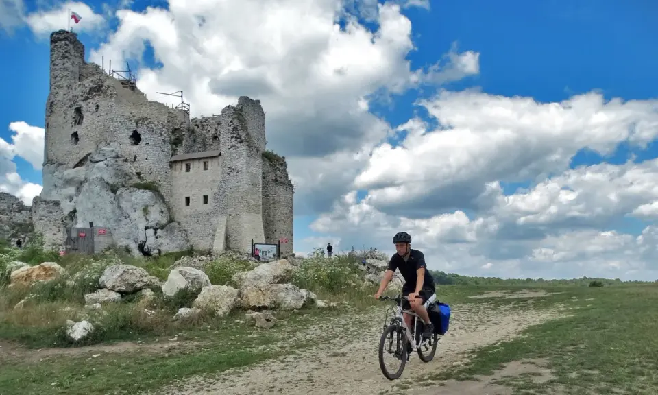 Rowerzysta na szlaku jura krakowsko częstochowska trasa, obok ruin zamku na skale.