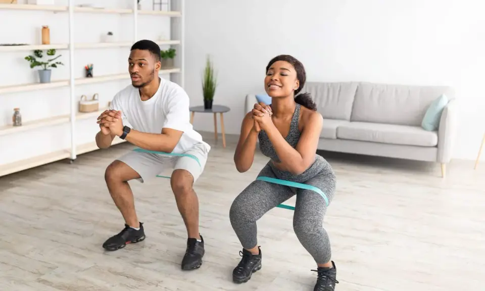 Pareja haciendo sentadillas con bandas elásticas para glúteos en casa.