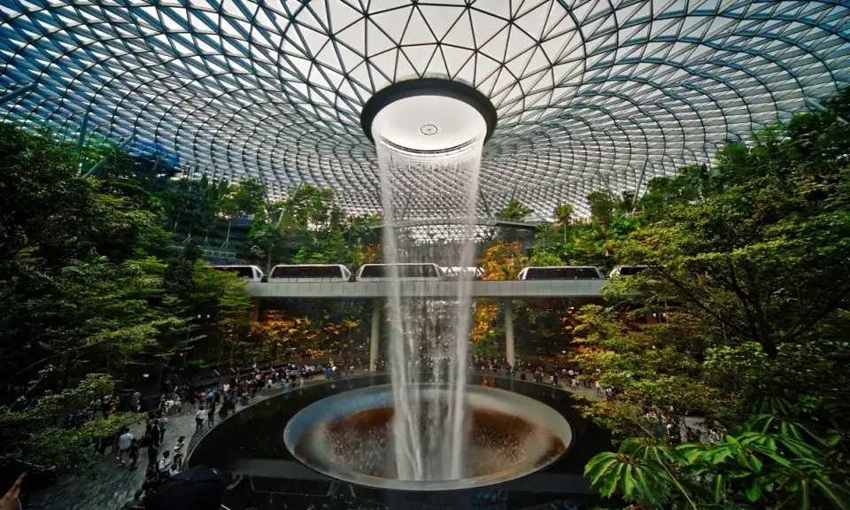 Wodospad HSBC Rain Vortex w porcie lotniczym Singapur-Changi, otoczony bujną zielenią i przejeżdżającymi pociągami.