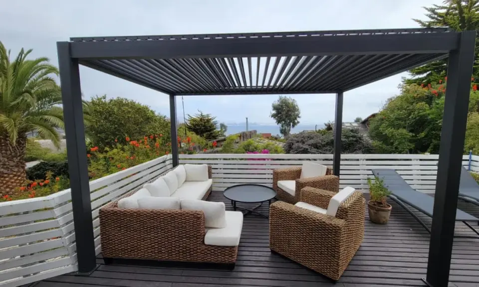 Un salon d'extérieur confortable sous une pergola sur toit terrasse, avec vue sur la mer.
