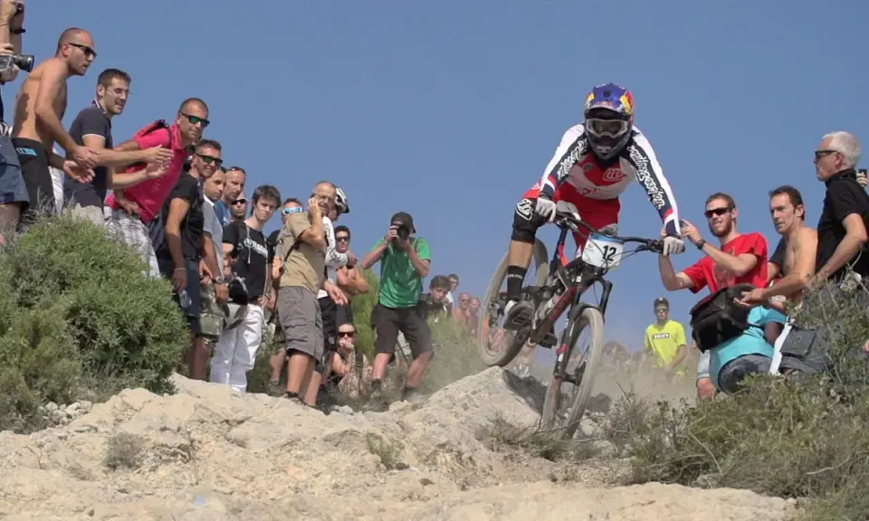 Kolarz w akcji podczas zawodów MTB, otoczony przez kibiców i fotografów.