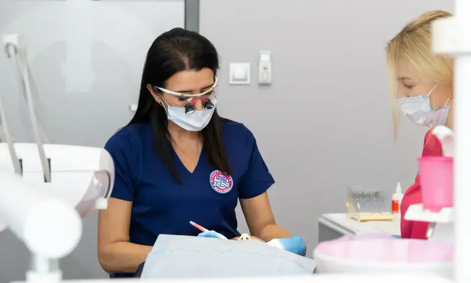 Dentystka w okularach i masce pracuje przy pacjencie. Dyskutują, jak przyspieszyć schodzenie znieczulenia.
