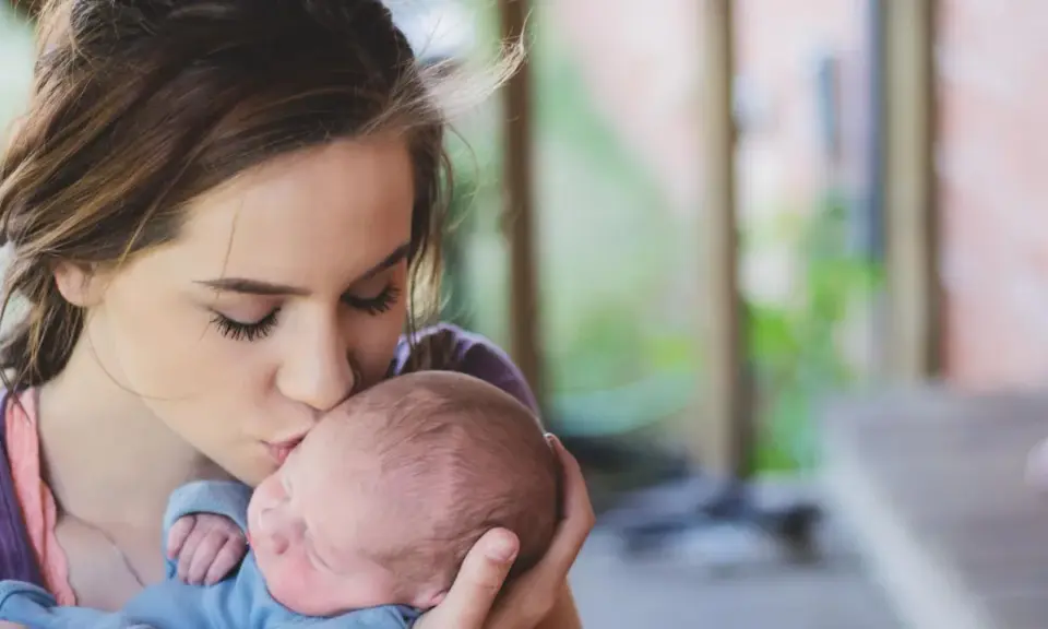 Une jeune femme, peut-être enceinte à 18 ans, embrasse tendrement son bébé.