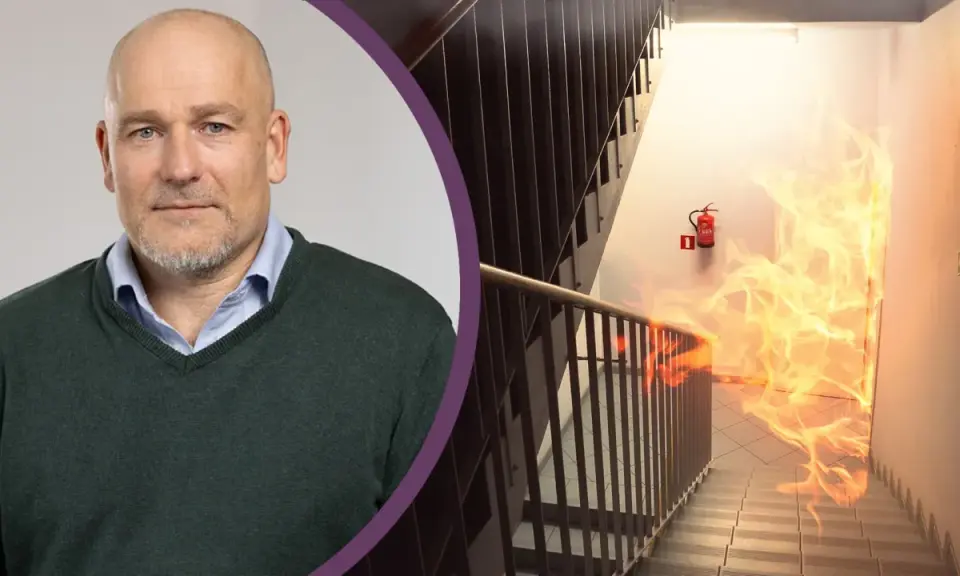 Man med skägg och en brandhärjad trappa med brandsläckare. Viktigt med revisionsbesiktning brandlarm för säkerheten.