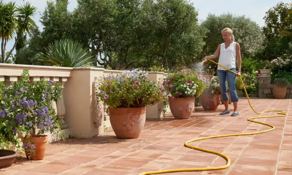 Mujer riega flores en macetas en una terraza, mostrando diferentes tipos de riego para mantenerlas sanas y vibrantes.