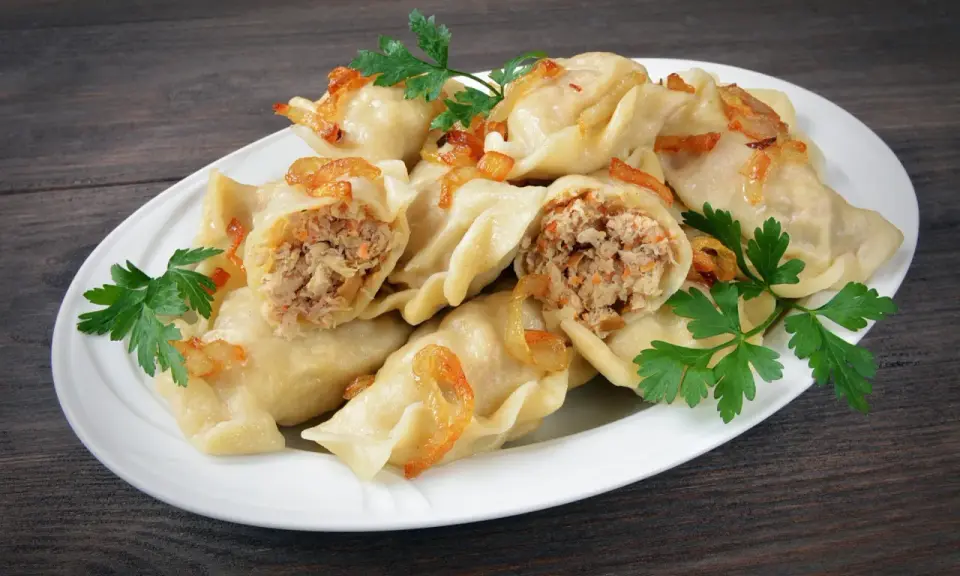 Pyszne pierogi z mięsem i kapustą, okraszone skwarkami i udekorowane natką pietruszki, na białym talerzu.