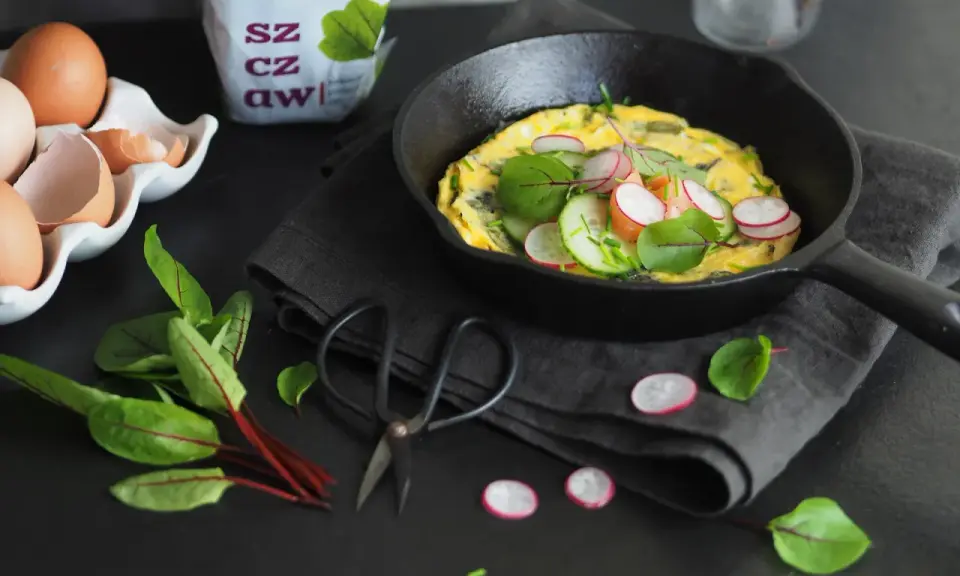Jak zrobić dobry omlet? Oto inspiracja: puszysty omlet z rzodkiewką, ogórkiem i ziołami na czarnej desce.