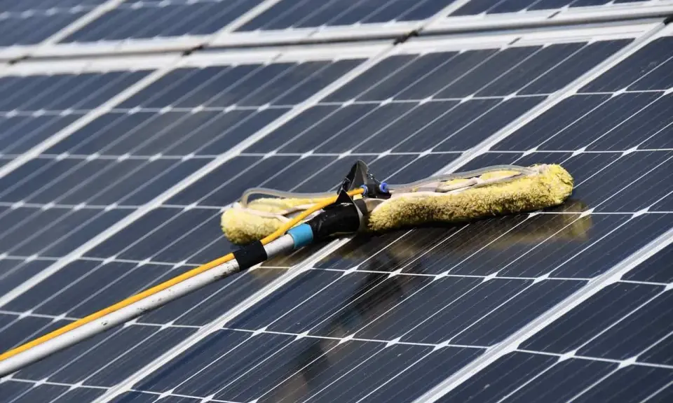 Reinigung von Solaranlagen mit einem Teleskopwischer. Gelber Wischerkopf auf dunklen Solarzellen.