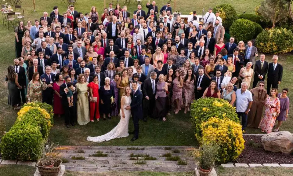 Una gran familia celebra una boda íntima al aire libre. Todos posan sonrientes para la foto grupal en un jardín verde.