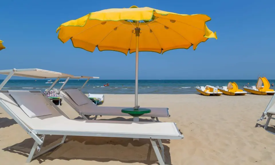 Lettini e ombrelloni gialli sui bagni Rimini, con pedalò gialli pronti per il mare azzurro.