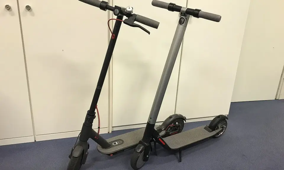 Deux trottinettes électriques, noires et grises, prêtes à l'emploi. La trottinette électrique définition : un moyen de transport urbain pratique.