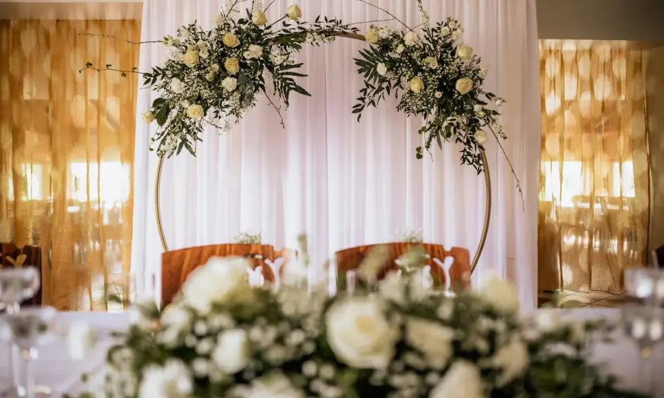 Elegancki ołtarz na ślub w plenerze, ozdobiony białymi kwiatami i zielenią na złotym okręgu.