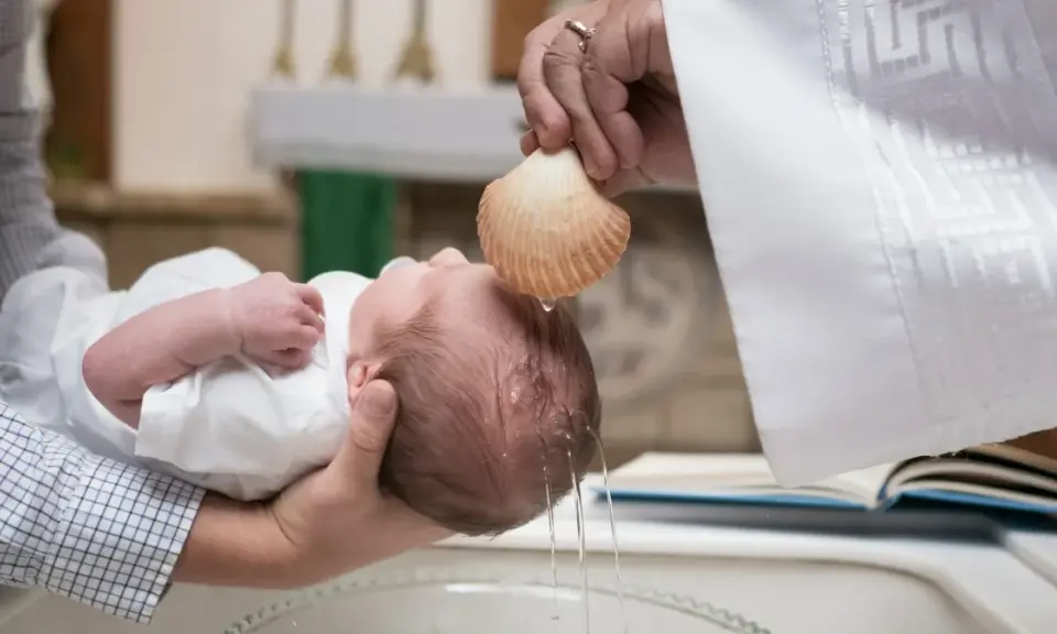 Chrzest dziecka. Kapłan polewa główkę niemowlęcia wodą święconą z muszli. To ważny moment, jak ile daje się na chrzciny.