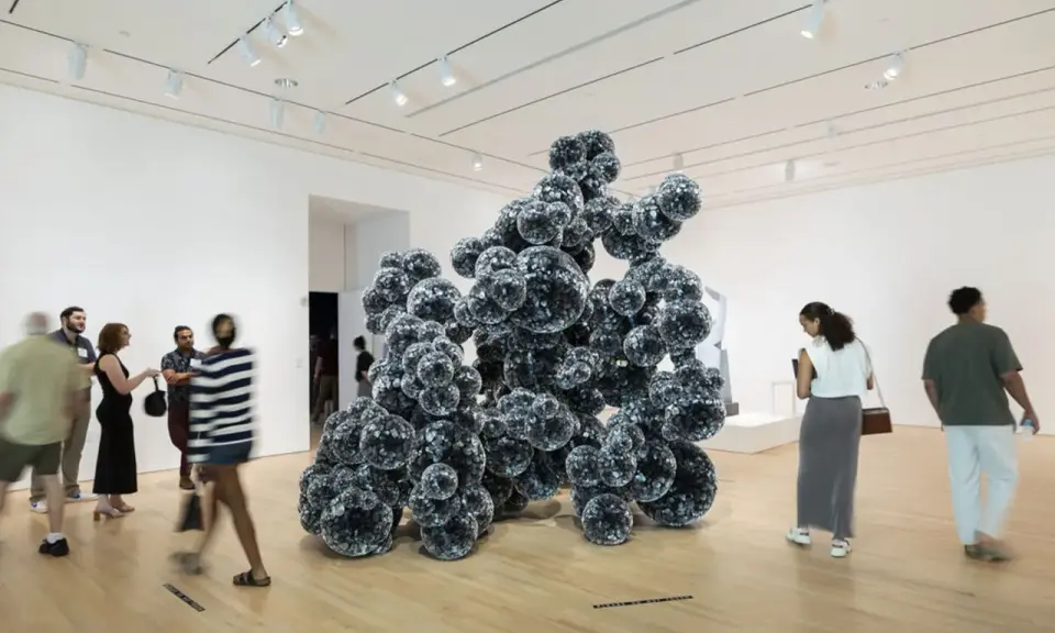 Visitors admire a large, dark, spherical sculpture in a bright gallery space, typical of Indianapolis Museum of Art photos.