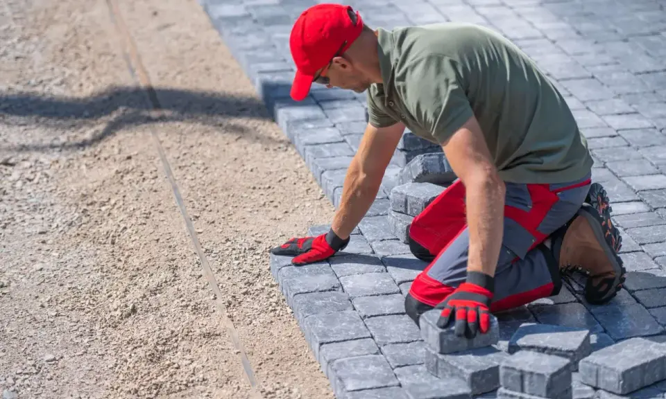 Pracownik w czerwonej czapce układa kostkę bauma na podsypce.
