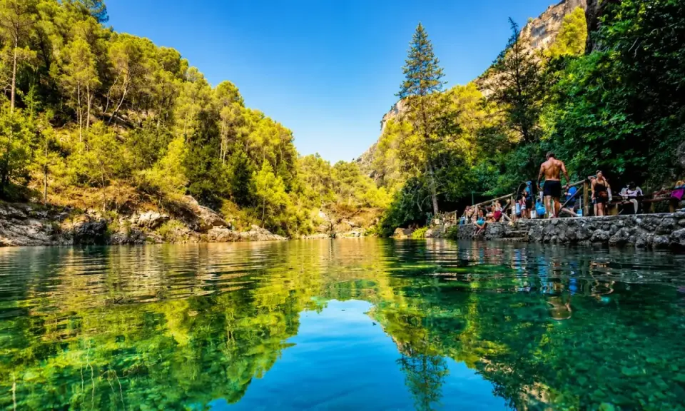 Un refrescante charco del aceite, rodeado de vegetación exuberante y rocas, con gente disfrutando del día.