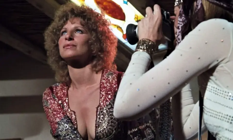 Barbra Streisand poses as Audrey Hepburn, dressed in a sparkly outfit, captures the moment with her camera.