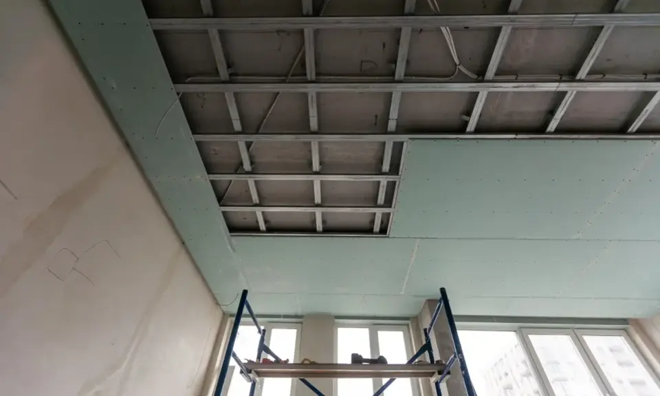 Instalación de falso techo de pladur para aislar techo ruido vecinos. Andamio y estructura metálica visibles.