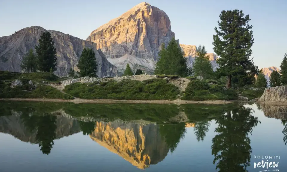 Riflesso perfetto di una montagna imponente nel lago di Limides, con alberi verdi e cielo azzurro.