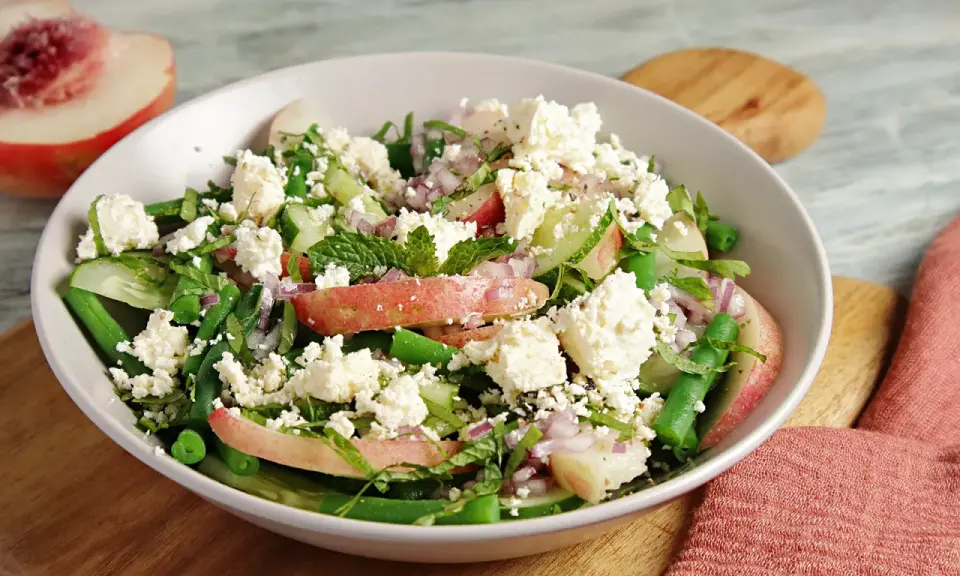Erfrischender Salat mit Nektarinenstücken, grünen Bohnen, Gurke, roten Zwiebeln und zerbröseltem Feta.