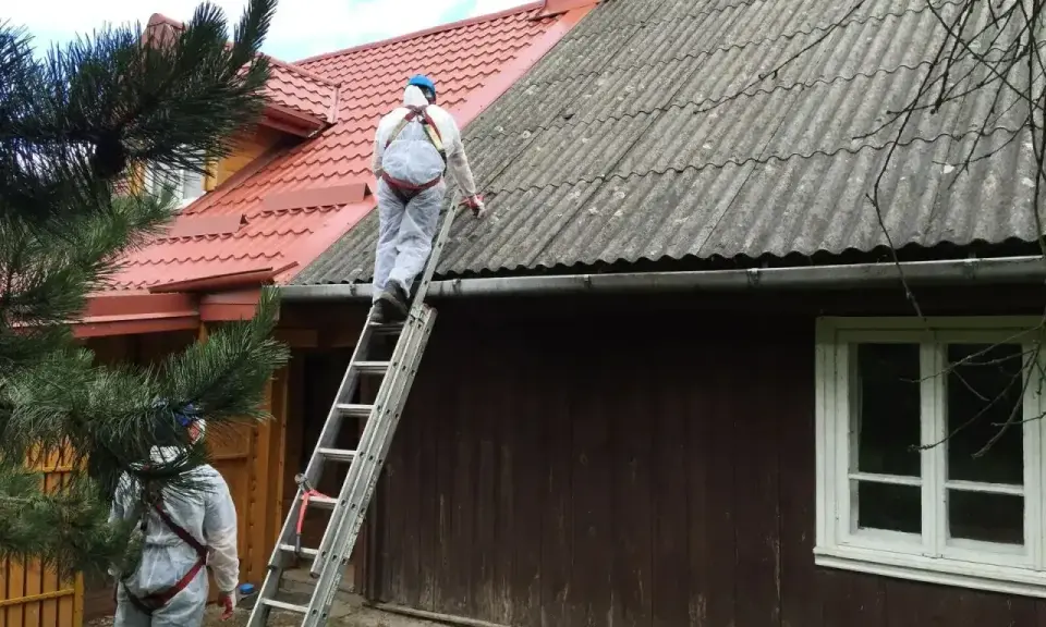 Pracownicy w kombinezonach zabezpieczających usuwają eternit z dachu. To pokazuje, co to jest azbest i jak wygląda jego utylizacja.