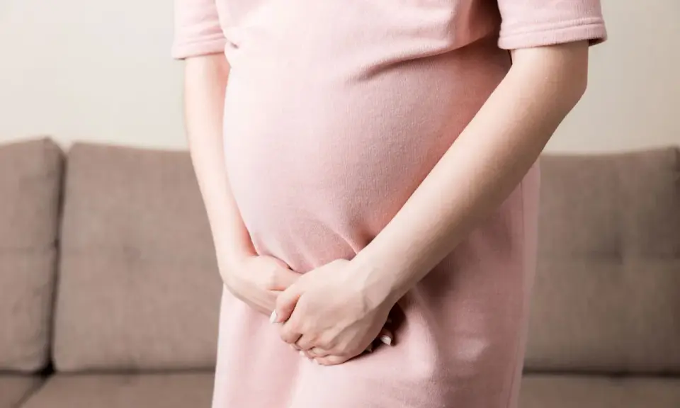 Kobieta w ciąży w różowej sukience trzyma ręce na brzuchu, doświadczając dyskomfortu związanego z nietrzymaniem moczu w ciąży.