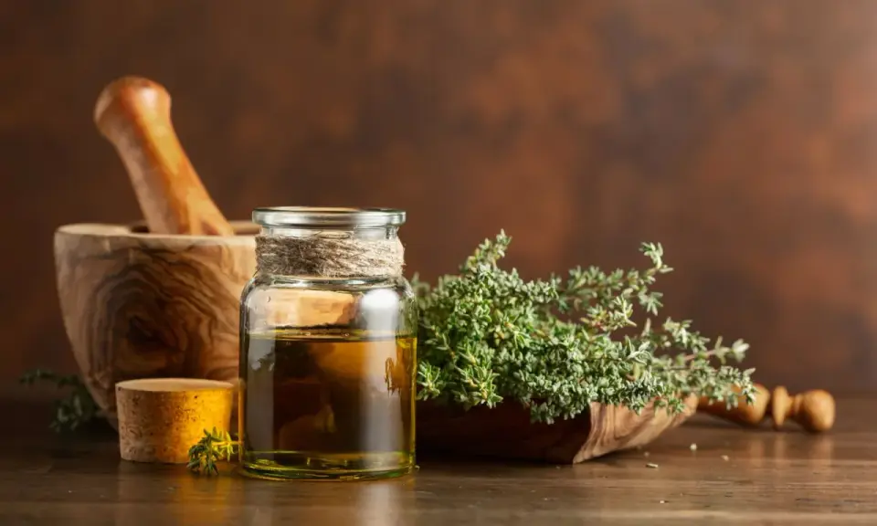 Olio essenziale timo proprietà: un flacone di vetro con olio dorato, un mortaio di legno e rametti di timo fresco.