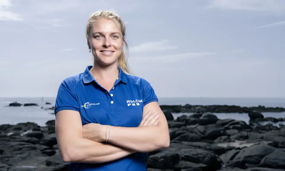 Rosalin Kuiper, souriante, pose les bras croisés devant un paysage côtier rocheux.