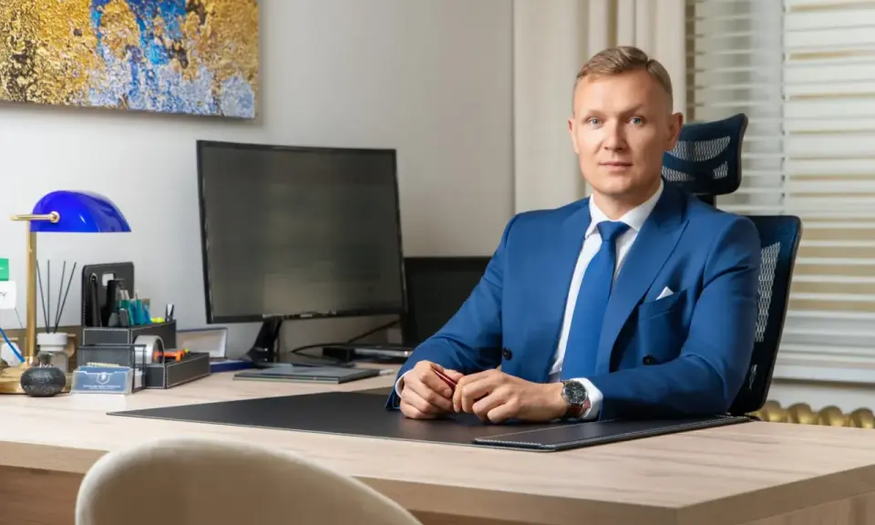 Mężczyzna w niebieskim garniturze siedzi przy biurku w nowoczesnym biurze.