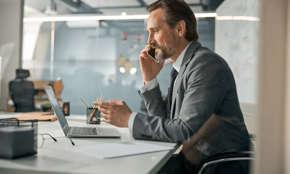 Mężczyzna w garniturze rozmawia przez telefon, pracując przy laptopie. To typowy dzień w pracy, nawet dla samego CEO.